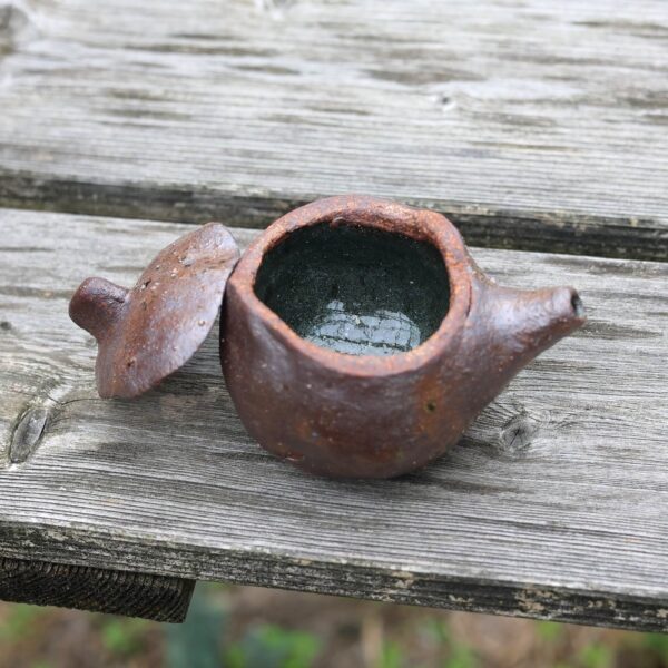 Une Mini Théière ref 9 rustique et faite à la main, mettant en valeur un art de la poterie exquis, est présentée avec son couvercle retiré et placé sur une surface en bois. - Atelier Terre et Bois à Colmar