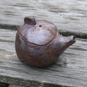 La Mini Théière réf 9, une théière rustique en argile texturée avec un bec court et une anse fabriquée par des artisans potiers qualifiés, repose sur une surface en bois. - Atelier Terre et Bois à Colmar