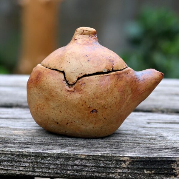 La Mini Théière réf 8, une théière ronde et rustique en terre cuite réalisée dans la tradition de la poterie fine, repose sur une surface en bois patiné, avec son bec verseur et son couvercle mettant en valeur l'art de l'artisanat. - Atelier Terre et Bois à Colmar