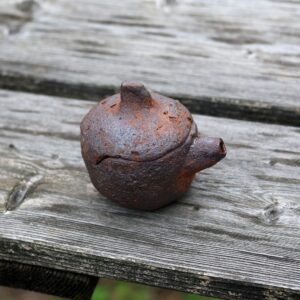 La Mini Théière réf 4, une petite théière en céramique de fabrication artisanale dotée d'un bec verseur et d'une anse, repose sur une surface en bois patiné. - Atelier Terre et Bois à Colmar