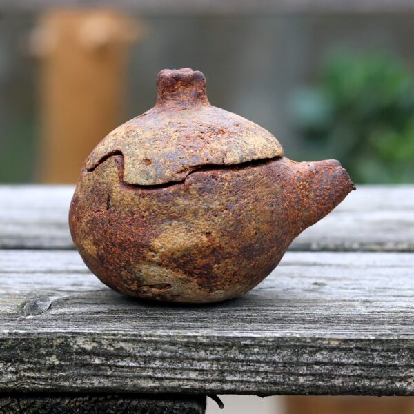 La Mini Théière réf 5, une théière ronde patinée et vieillie rappelant la poterie traditionnelle, avec un petit bec verseur, repose sur un plateau extérieur en bois. - Atelier Terre et Bois à Colmar