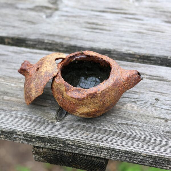 La Mini Théière réf 5, une théière en métal rouillée et cassée avec un couvercle détaché, repose sur une surface en bois patiné, capturant l'essence de l'artisanat vieilli dans sa conception complexe. - Atelier Terre et Bois à Colmar