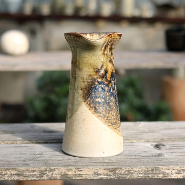 Un vase en céramique à glaçure texturée et multicolore repose sur une surface en bois rappelant le Pichet en grès - sans anse réf 22. - Atelier Terre et Bois à Colmar