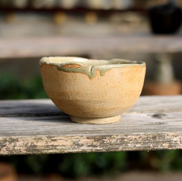 Le Bol en grès - réf 61, un bol en céramique fabriqué à la main avec une glaçure irrégulière qui met en valeur la poterie et l'artisanat exquis, repose sur une surface en bois à l'extérieur. - Atelier Terre et Bois à Colmar