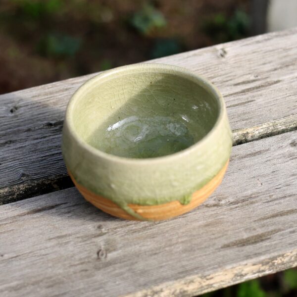 Le Bol à matcha en grès - réf 75, petit bol en céramique verte orné d'un émail craquelé et mettant en valeur un artisanat céramique exceptionnel, repose sur une surface en bois patiné. - Atelier Terre et Bois à Colmar