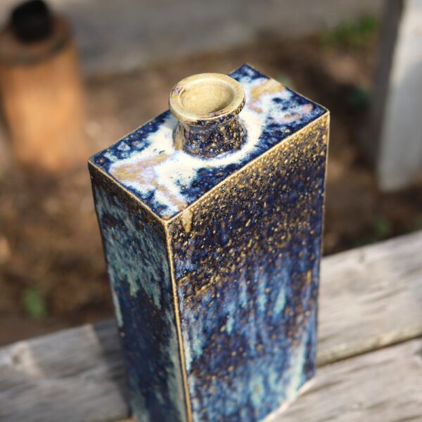 Présentation extérieure du Grand vase rectangulaire en grès - Blanc - Bleu - réf 4, avec une ouverture étroite et une glaçure céramique texturée bleue et beige, mettant en valeur un savoir-faire exquis sur une surface en bois. - Atelier Terre et Bois à Colmar