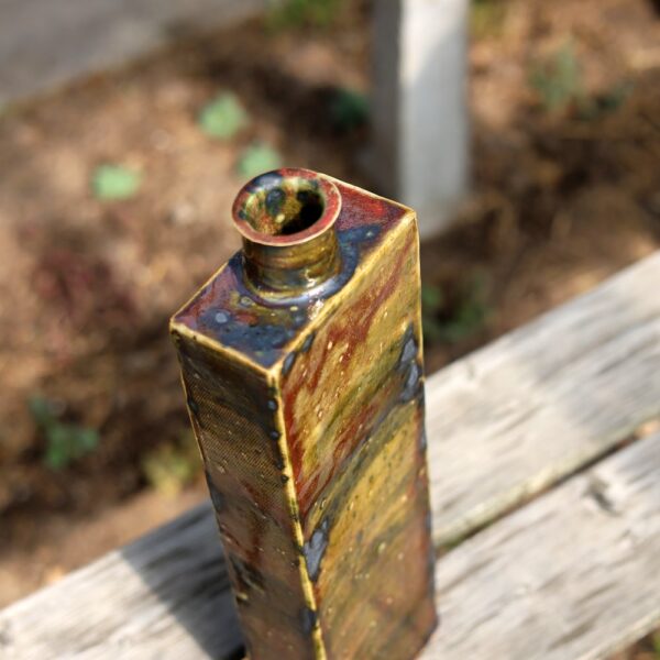 Le Grand vase rectangulaire en grès - vert - rouge - réf 5, doté d'une petite ouverture ronde et d'une glaçure tachetée de teintes brunes et vertes qui met en valeur l'artisanat de poterie exquis, repose sur une surface en bois à l'extérieur. - Atelier Terre et Bois à Colmar