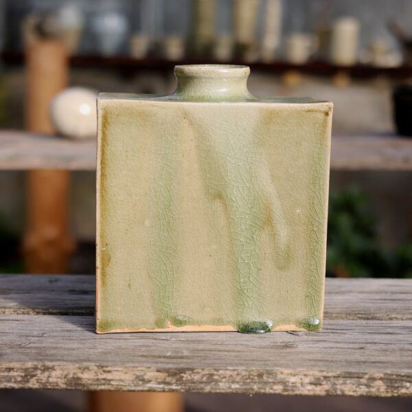 Le Vase rectangulaire en grès - réf 9, doté d'une glaçure vert clair avec un motif craquelé visible, met en valeur un artisanat exquis et est élégamment présenté sur une surface en bois. - Atelier Terre et Bois à Colmar