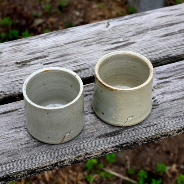 Le Duo de petites tasses en grès avec décoration gravée, deux tasses en céramique simples et rustiques avec un vernis gris clair, fabriquées avec l'art de la poterie et céramique, reposent élégamment sur une surface en bois patiné. - Atelier Terre et Bois à Colmar