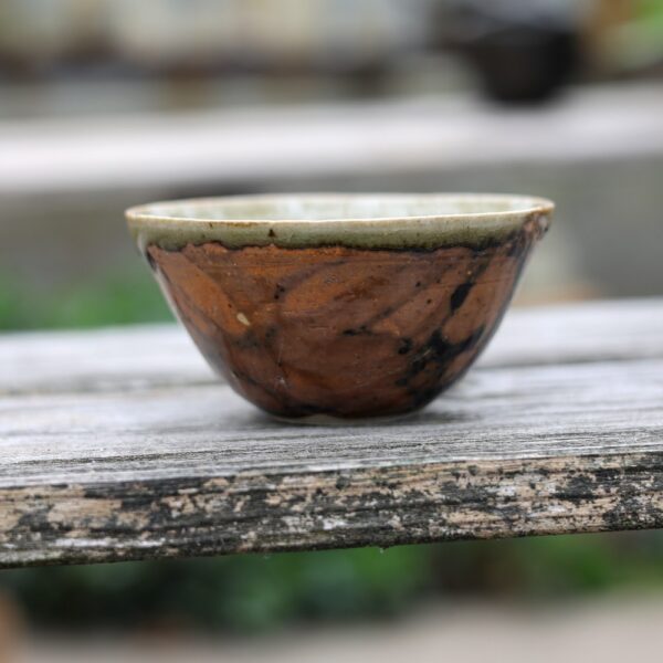 Un bol en céramique avec un motif tourbillonnant brun et foncé est posé sur une surface en bois à l'extérieur, mettant en valeur l'art de la poterie fine. - Atelier Terre et Bois à Colmar