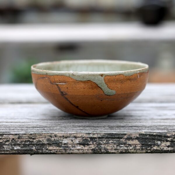 La Tasse artisanale en grès réf 62, avec ses fissures visibles et ses élégantes réparations dorées, repose fièrement sur une surface en bois patiné, illustrant l'art des techniques céramiques traditionnelles. - Atelier Terre et Bois à Colmar