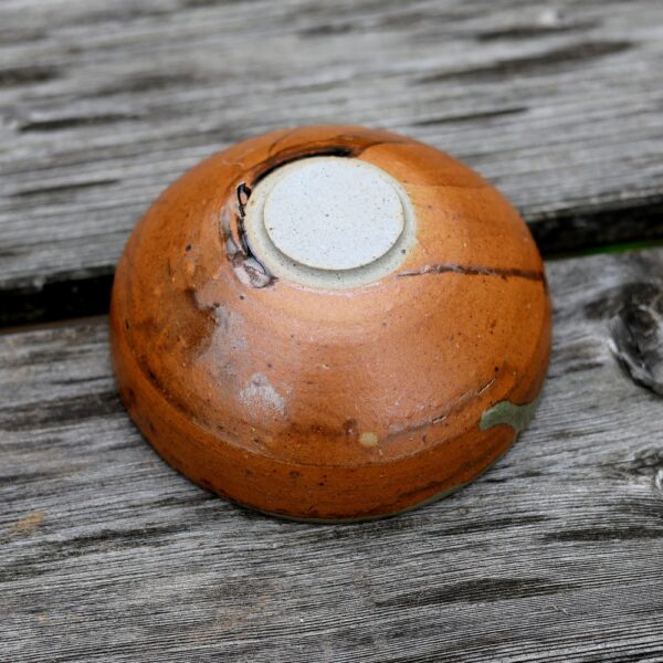 Une "Tasse artisanale en grès réf 62" distinctive de couleur marron est posée à l'envers sur une surface en bois patiné. - Atelier Terre et Bois à Colmar